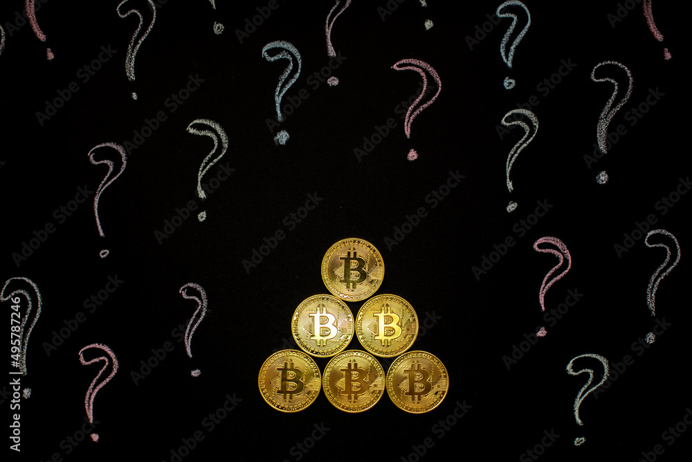 Fototapeta premium Hand holding Bitcoin virtual money against blackboard with question marks.