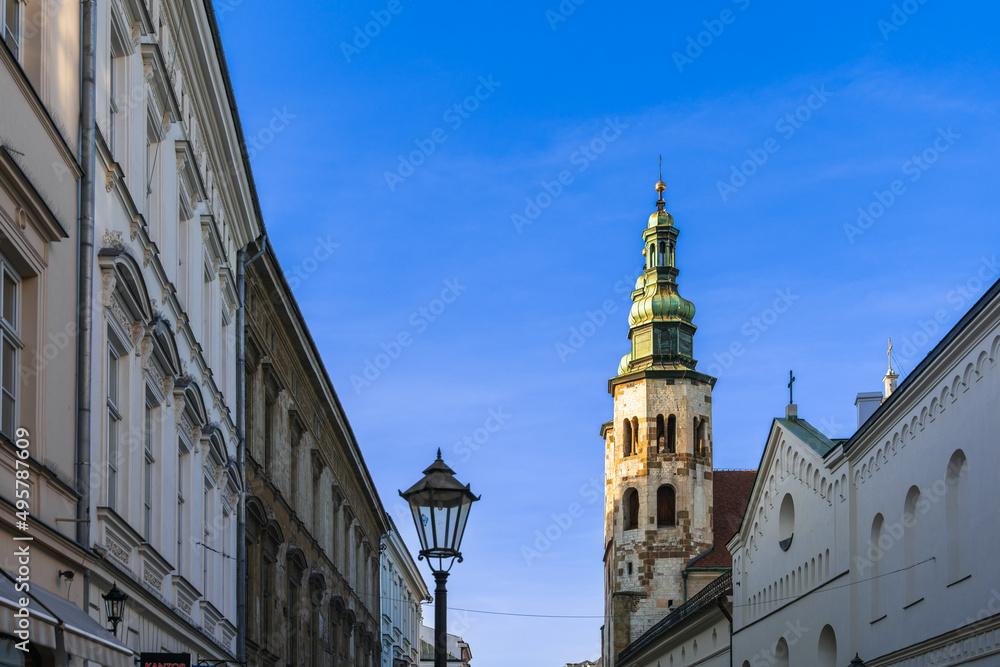 Vintage houses, street lamp, tall gothic tower of the catholic church at sunset in the rays of the evening sun against the blue sky in the spring in Krakow