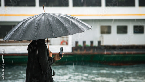 Photography Male traveler holding his smartphone by the sea on a rainy day