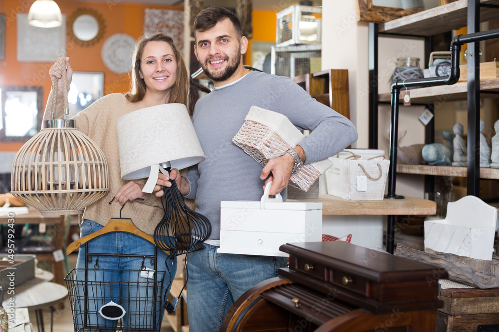 Portrait of happy young pair standing with purchases in furnishings shop.