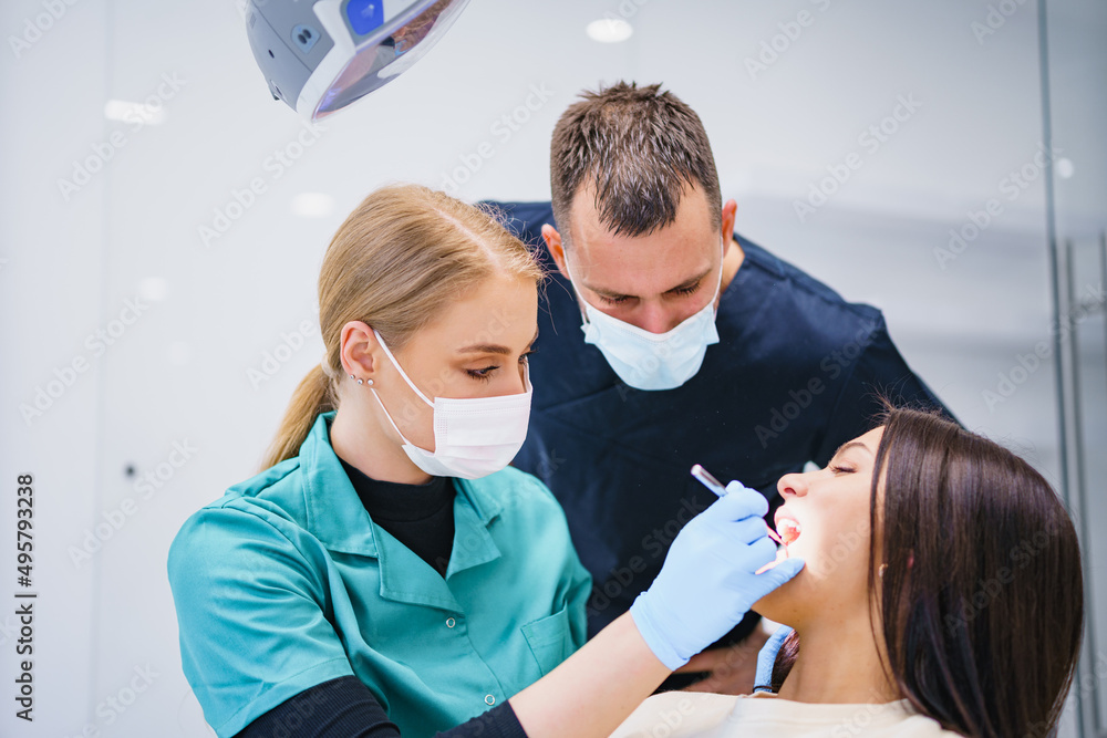 Two dentists examine and repair the patient's teeth. Three people in the dental office.