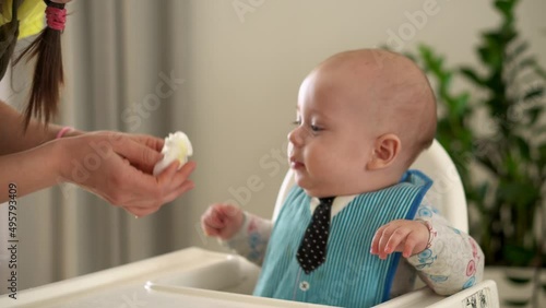 mom Mother feed young baby in white feeding up high chair, first supplement vegetable puree Happy smiling kid eat for the frst time, child with dirty face, little infant boy eating porridge nutrition photo