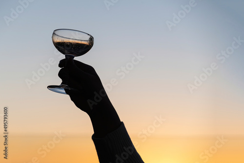 Silhouette of a hand holding a winecup to the sky at sunset photo