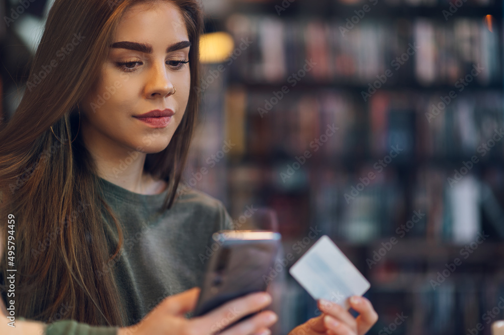 Woman using smartphone and a credit card for online shopping in a cafe Woman using smartphone and a credit card for online shopping in a cafe