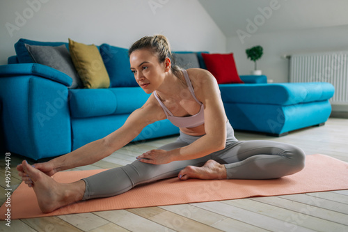Woman training at home and stretching leg while sitting on a fitness mat