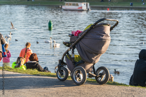 A baby stroller stands on an asphalt road near the river bank in the rays of evening sunlight