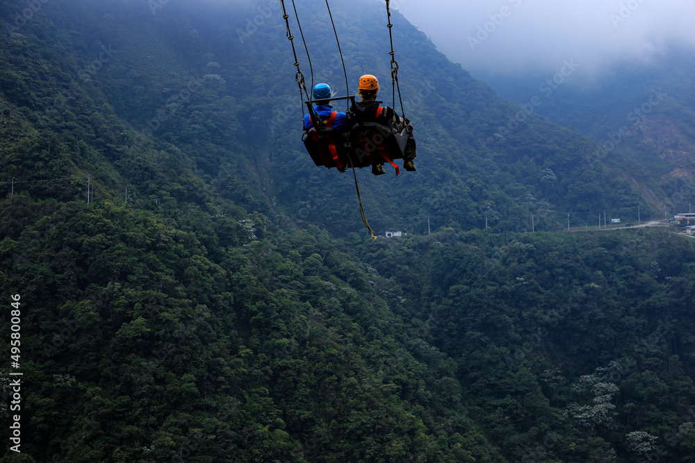 Obraz premium Two tourist are relaxing in a giant swing with a mountain and forest in the background: a famous tourist attraction which swings over a raving or canyon in Ecuador