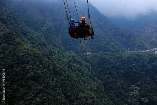 Two tourist are relaxing in a giant swing with a mountain and forest in the background: a famous tourist attraction which swings over a raving or canyon in Ecuador