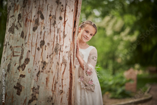 Communion girl posing next to a big tree in a park photo