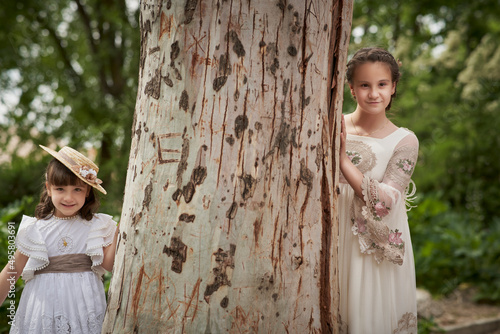 Communion girl posing with her sister next to a large tree photo