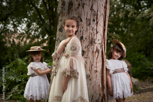 Communion girl posing with her twin little sisters in a park photo