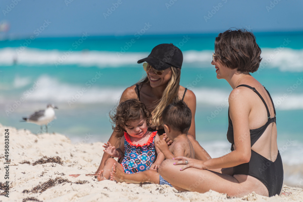 Two young latin moms posing with their toddlers at a caribbean beach Two young latin moms posing with their toddlers at a caribbean beach