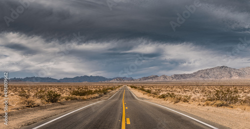 Panorama of desert highway in leading to mountains under a dark stormy sky; concepts of adventure, uncertainty, future, travel 