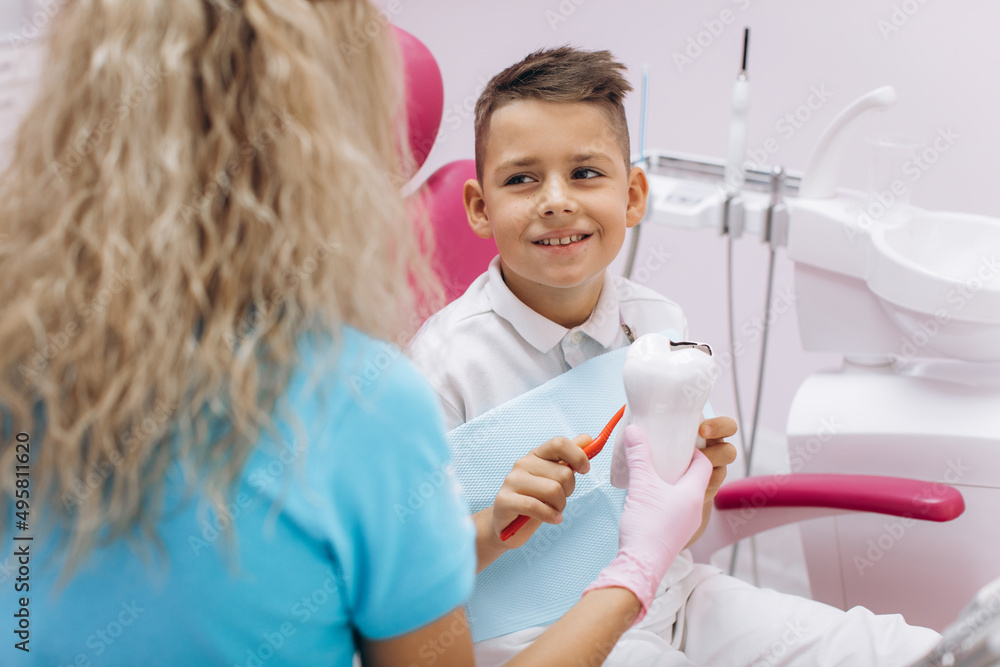 Female dentist shows a boy on a mock-up how to brush his teeth properly Female dentist shows a boy on a mock-up how to brush his teeth properly