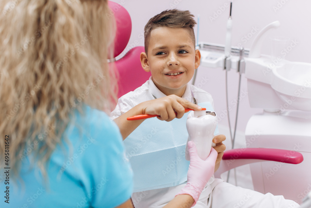 Female dentist shows a boy on a mock-up how to brush his teeth properly Female dentist shows a boy on a mock-up how to brush his teeth properly