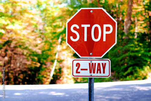 Red 2 way stop sign against road traffic and autumn nature trees. Public transport and traffic control, stop sign background.