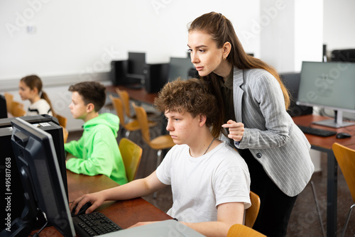 Teacher explaining task solution to teenage boy during computer science lesson in school.