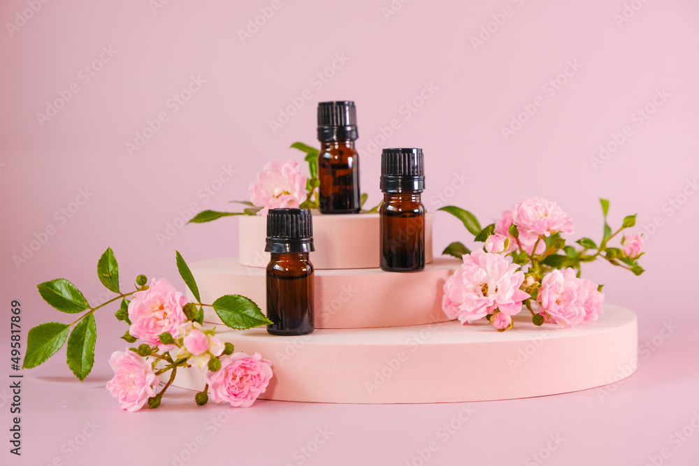 Rose essential oil.Aromatherapy and cosmetics. Glass brown bottles set and pink rose flowers on a pink podium on light pink background.Organic natural rose oil.Organic bio cosmetics.Rose oil Rose essential oil.Aromatherapy and cosmetics. Glass brown bottles set and pink rose flowers on a pink podium on light pink background.Organic natural rose oil.Organic bio cosmetics.Rose oil