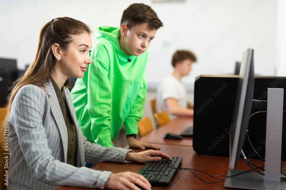 Smart focused tween schoolboy helping young puzzled woman working with computer in public library. Generation Z or digital natives concept