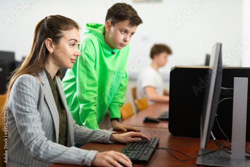 Obraz na plátně Smart focused tween schoolboy helping young puzzled woman working with computer in public library