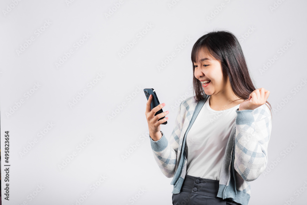 Woman excited holding mobile phone funky successful raise fists say yes! studio shot isolated white background, happy young female smiling surprised make winner gesture on smartphone Woman excited holding mobile phone funky successful raise fists say yes! studio shot isolated white background, happy young female smiling surprised make winner gesture on smartphone