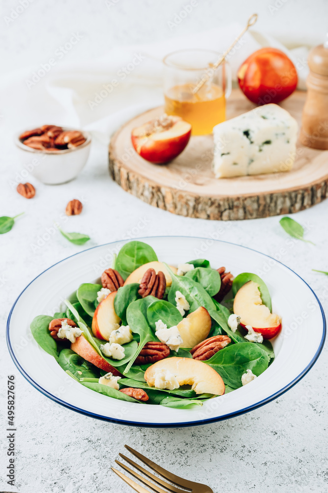 Healthy summer salad with spinach, peach, pecan nuts, blue cheese on white background Healthy summer salad with spinach, peach, pecan nuts, blue cheese on white background