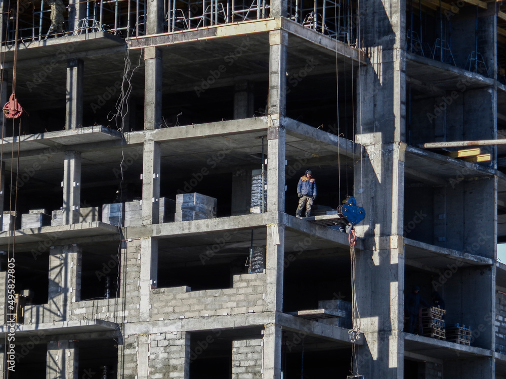 Building under construction. Kazakhstan (Ust-Kamenogorsk). Residential building. Construction crane. Cranes and building. New residential area. Construction site. Concrete frame. Monolith. Worker