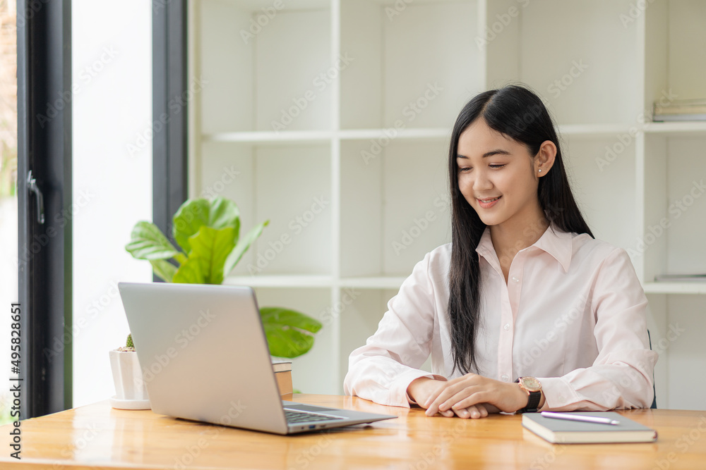 Portrait of a happy Asian woman smiling happily relaxing sitting on a chair. Independent young Asian hipster girl using laptop computer in coffee shop work-study concept