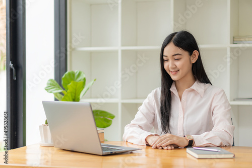 Portrait of a happy Asian woman smiling happily relaxing sitting on a chair. Independent young Asian hipster girl using laptop computer in coffee shop work-study concept