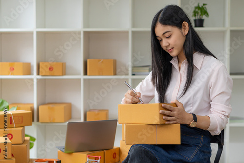 portrait of an Asian woman attractive girl sme business owners starts working with laptop happily with the box at home Prepare to deliver parcels in SMEs, supply chains, online procurement concepts. photo