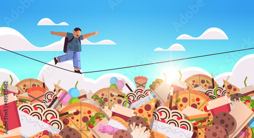 schoolboy balancing on rope above junk food assortment of fast food unhealthy nutrition junkfood addiction concept