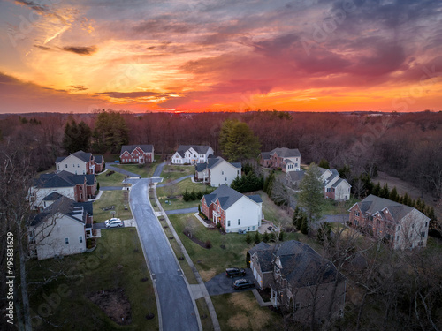 Aerial view of meticulous landscaping around colonial homes with brick front homesites in a cul-de-sac in Maryland with dramatic colorful sunset sky