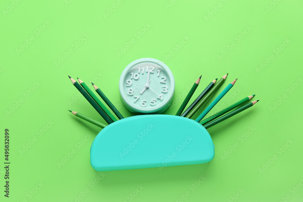 Case with color pencils and alarm clock on green background Case with color pencils and alarm clock on green background
