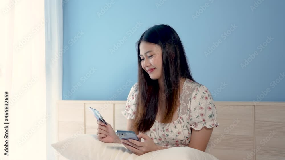 4K 50fps,Beautiful Asian girl, shopping online via mobile phone on a white bed, he sits happily looking at the credit card, when the credit card payment is successful,online shopping. 4K 50fps,Beautiful Asian girl, shopping online via mobile phone on a white bed, he sits happily looking at the credit card, when the credit card payment is successful,online shopping.