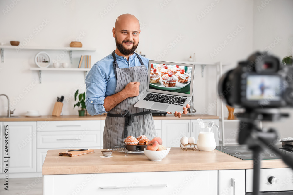 Handsome man with laptop and peach muffins in kitchen