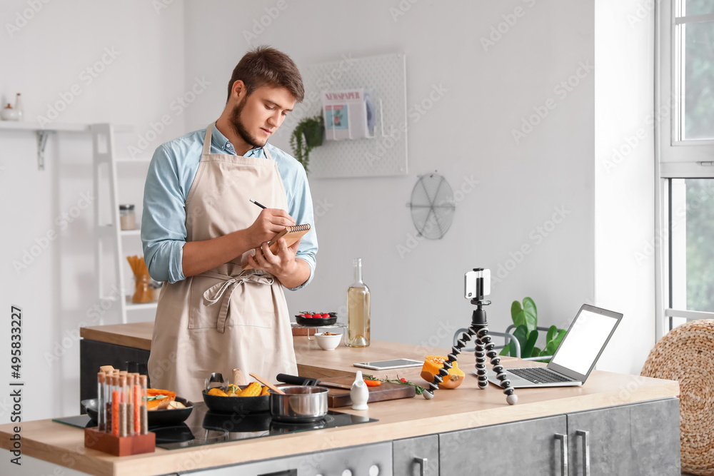 Young man making notes from cooking video tutorial in kitchen Young man making notes from cooking video tutorial in kitchen