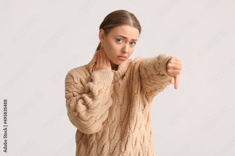 Ill young woman with sore throat showing thumb-down on light background Ill young woman with sore throat showing thumb-down on light background