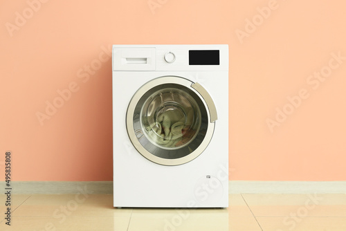 Modern washing machine with laundry near wall