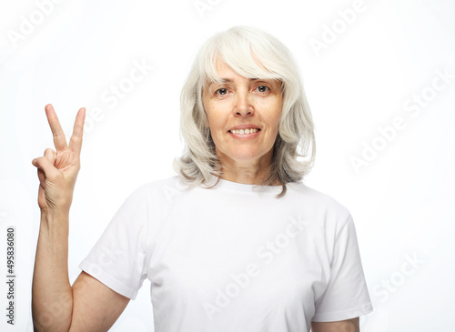 Old lady wearing white casual t-shirt showing v-sign victory peace gesture