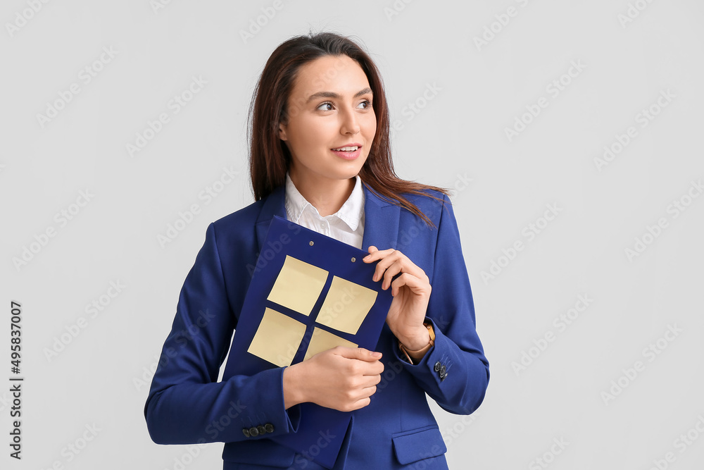 Young woman with sticky note papers on clipboard against light background Young woman with sticky note papers on clipboard against light background