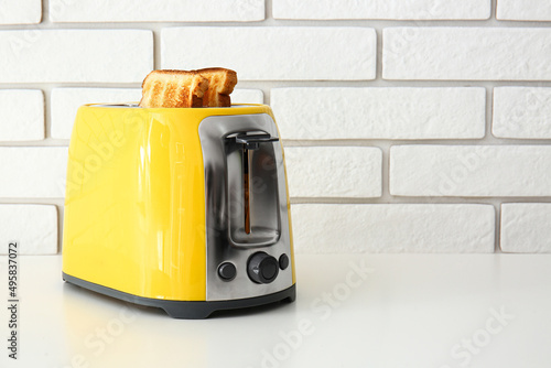 Modern toaster with bread slices on light table