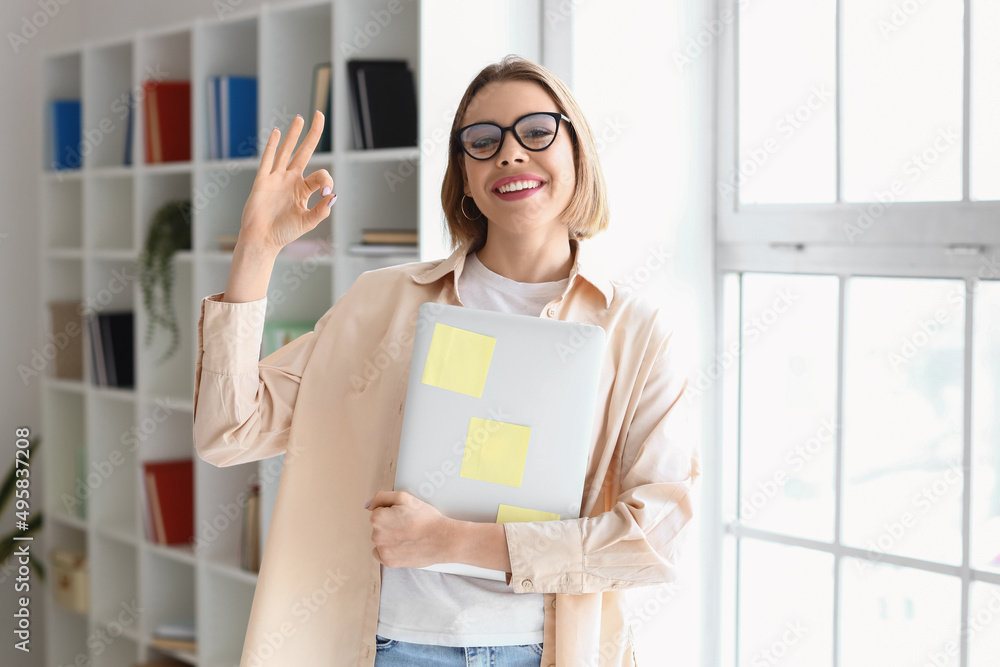 Female student with laptop showing OK in library