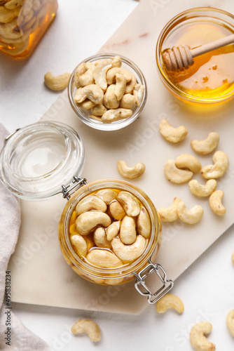 Jar of tasty cashew nuts with honey on light background