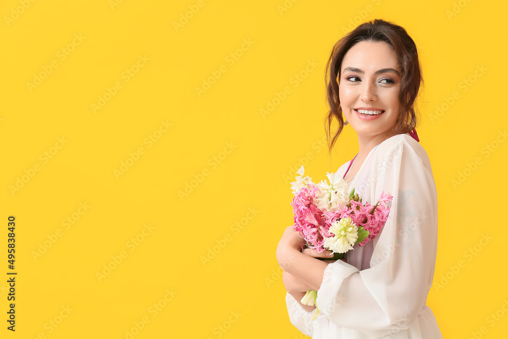 Pretty young woman with hyacinth flowers on yellow background