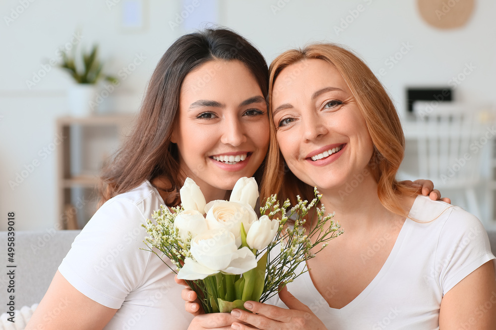 Young woman and her mother with flowers on International Women's Day at home