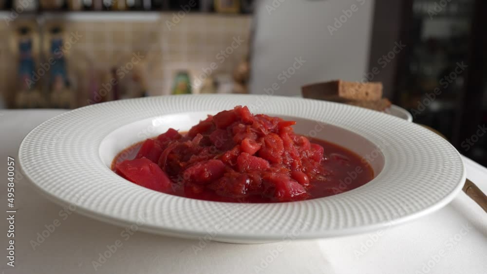 Traditional Ukrainian red soup or borscht with red beetroot, potato, carrot, cabbage, beans on the white bowl, close up. Plate of red beetroot soup borsch rotates on table. Traditional Ukraine food Traditional Ukrainian red soup or borscht with red beetroot, potato, carrot, cabbage, beans on the white bowl, close up. Plate of red beetroot soup borsch rotates on table. Traditional Ukraine food