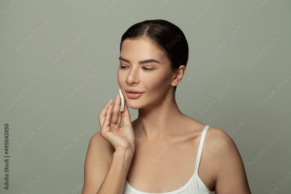 Fototapeta premium Attractive woman removing makeup with white cotton pad on gray background