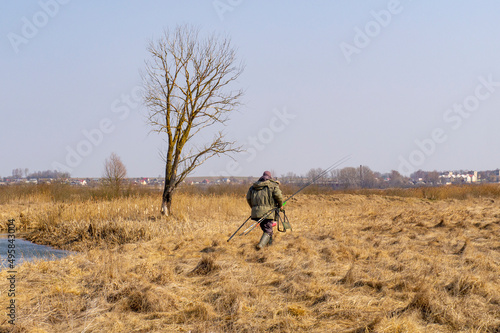 A tall male fisherman with fishing rods walks on the shore