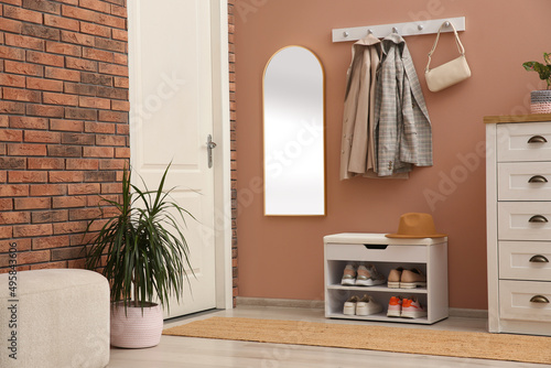 Rack with different shoes near pale pink wall in hall photo