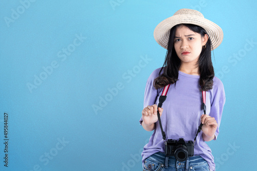 Asian woman with hat and camera standing with unhappy expression